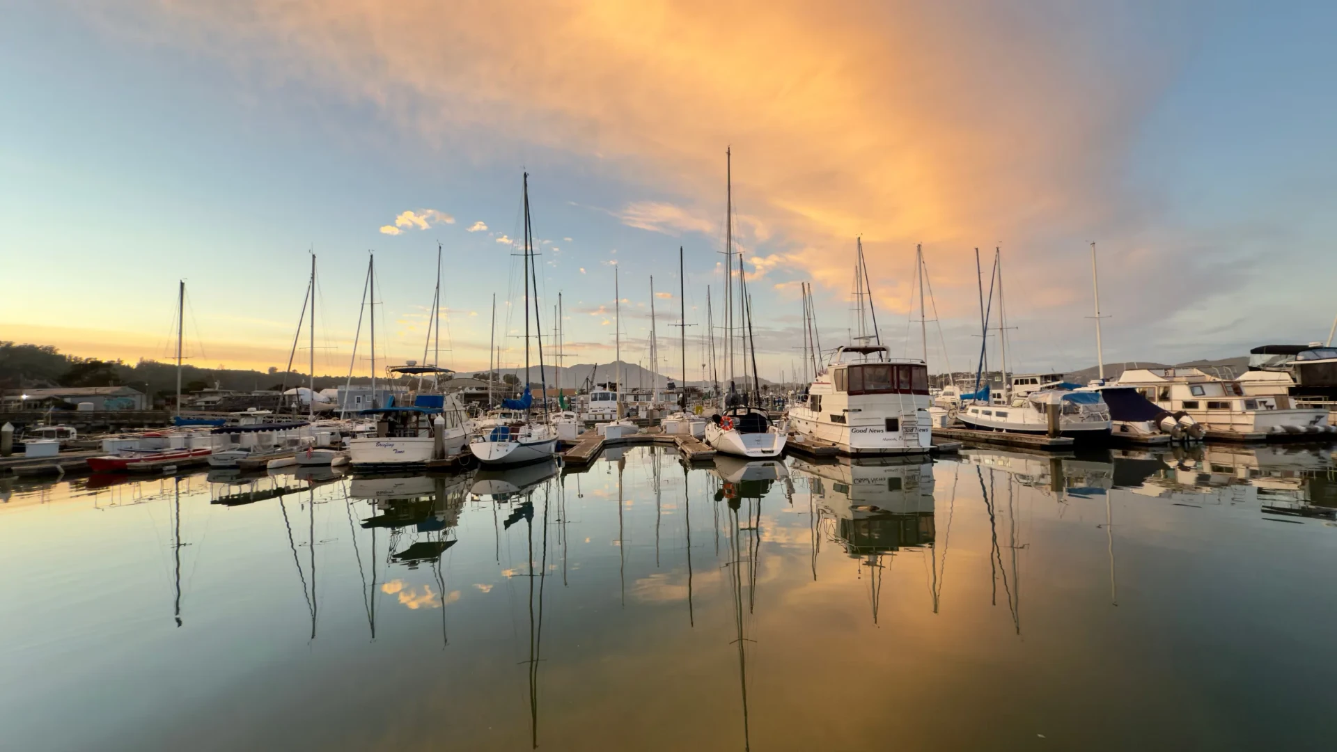 Sailboats and powerboats moored in a Sausalito marina at sunset with mirror-calm reflections
